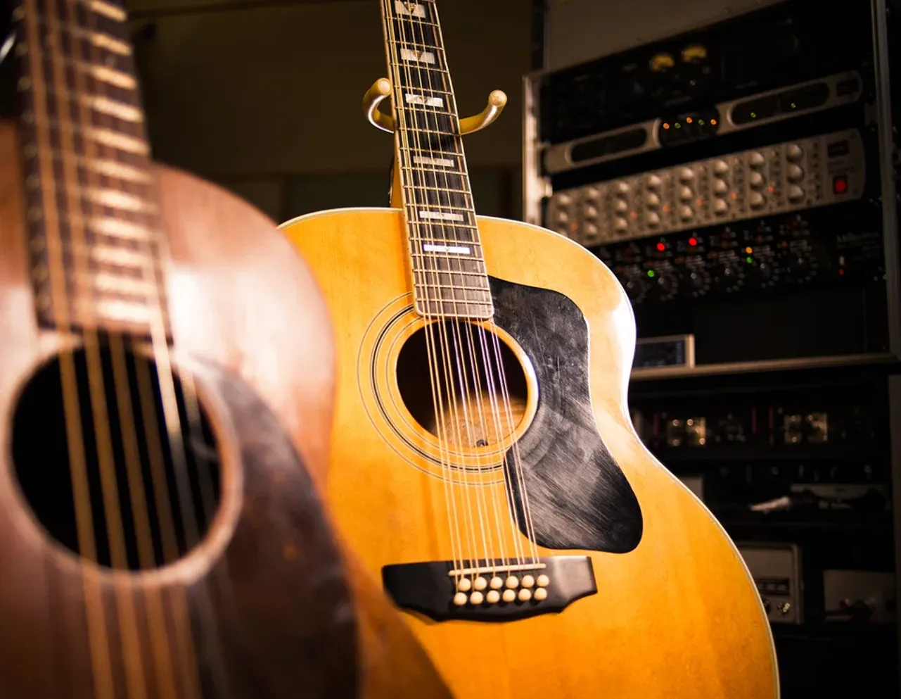 Two vintage acoustic guitars standing in a studio, a blonde twelve-string in front of a darker six-string.