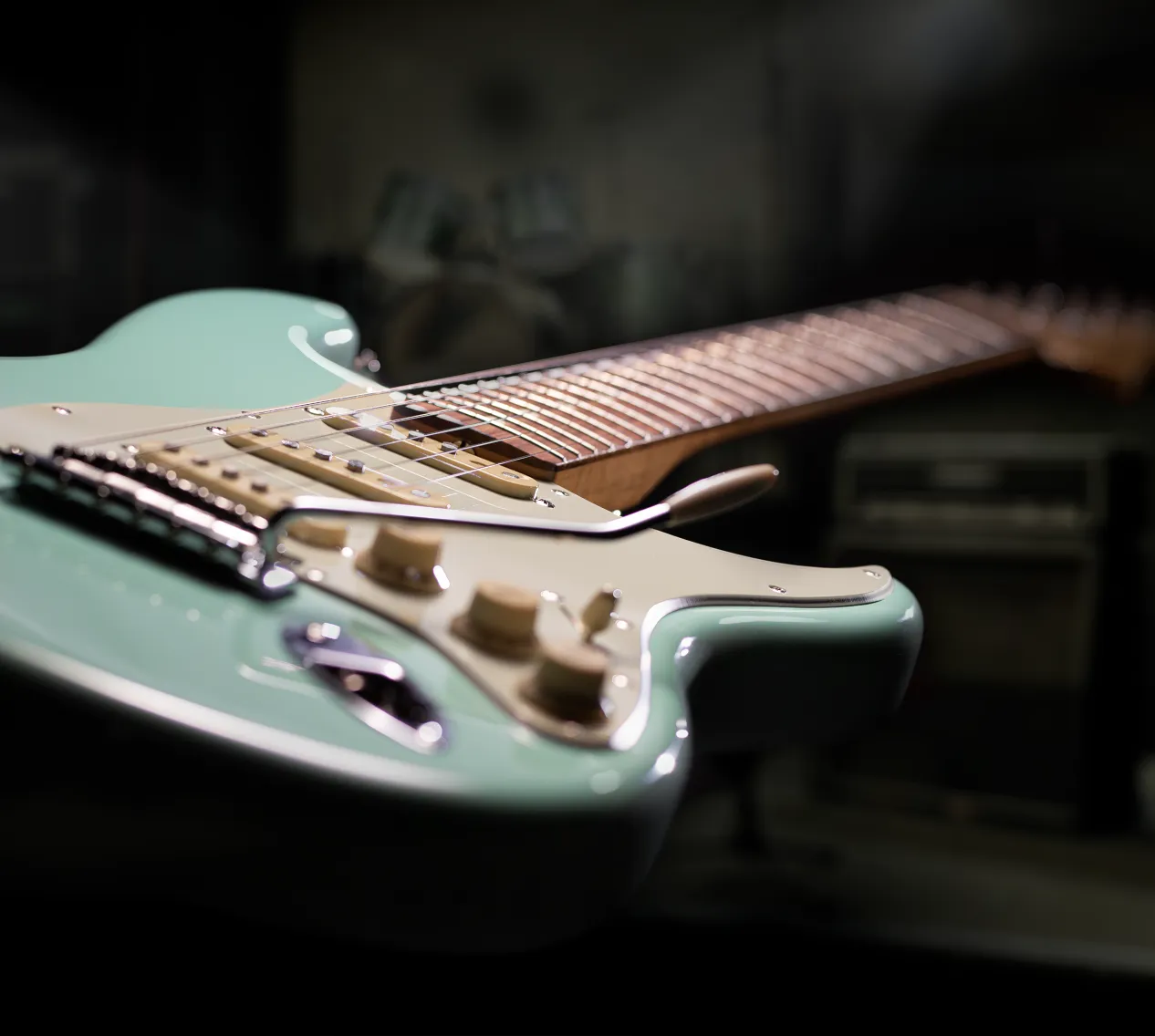 Close-up of a vintage solid-body electric guitar in mint finish, lit in a dark studio room.