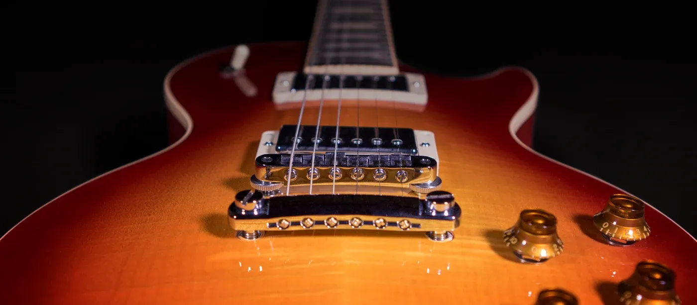 Close-up of a cherry sunburst electric guitar against black, the bridge, pickup and gold control knobs in focus.