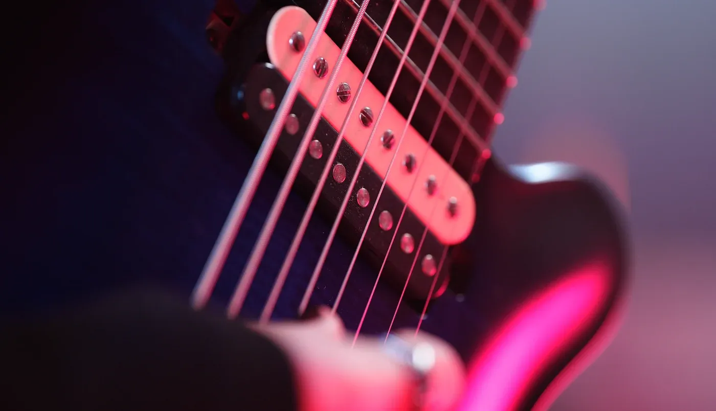 Close-up of an eight-string electric guitar's pickup and strings under magenta stage light.
