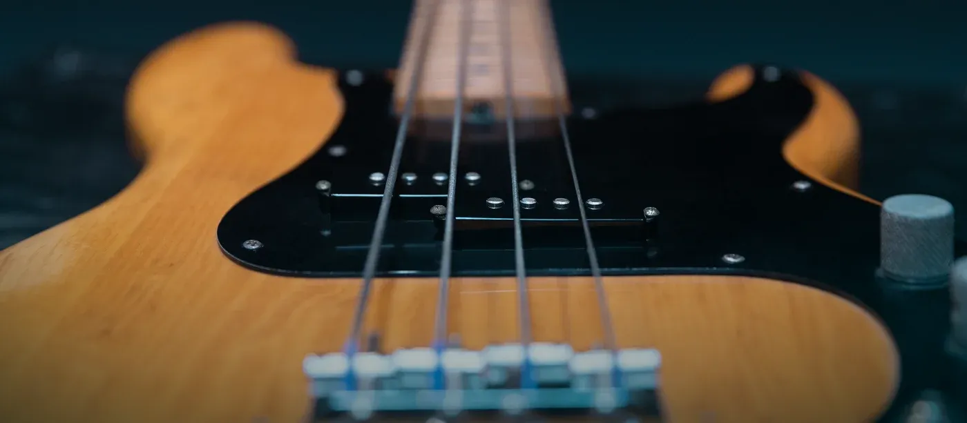 A natural-finish ash bass photographed along the strings, its black pickguard, split pickup and maple fingerboard in frame.