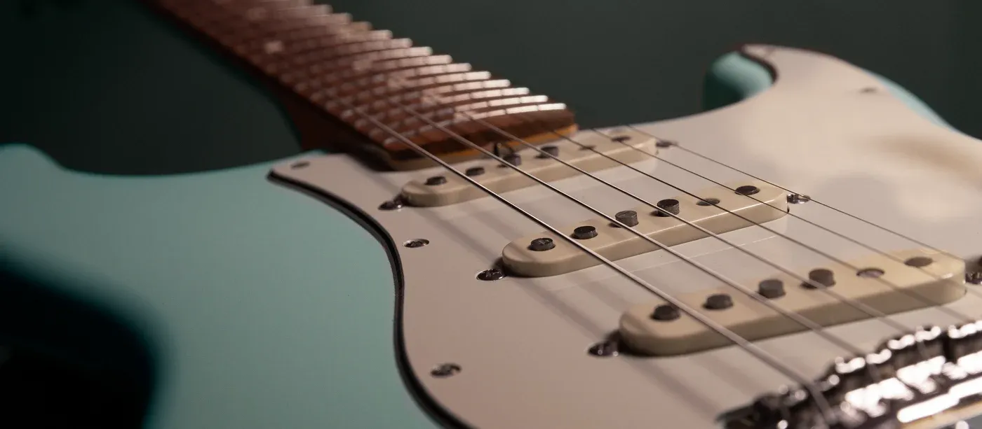 Detailed view of an electric guitar body and strings with a mint finish and cream pickguard.