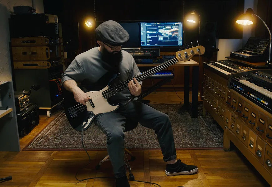 A bass player recording in the studio, surrounded by outboard racks and synths.